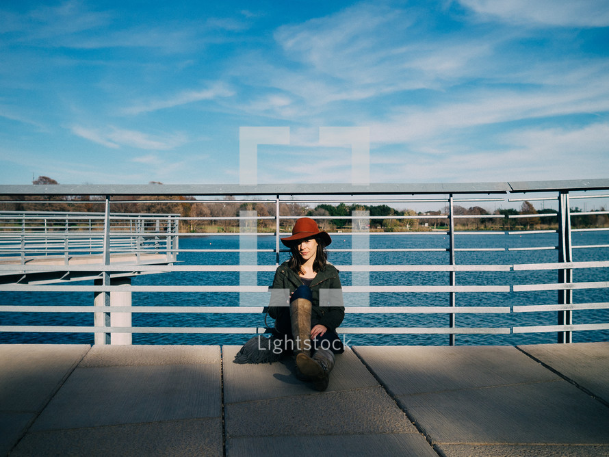 A woman in a red hat leans against a railing by a lake.