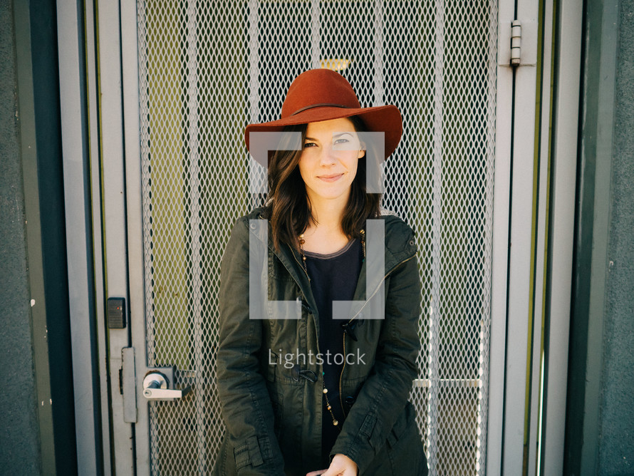 A woman in a red hat stands in front of a metal grid door.