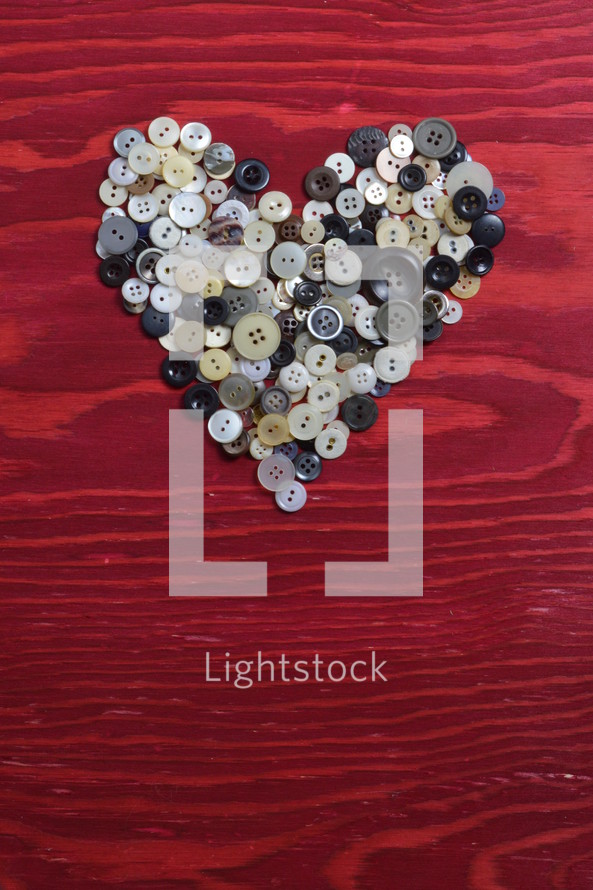 many little buttons shaping a heart on a red wooden background
