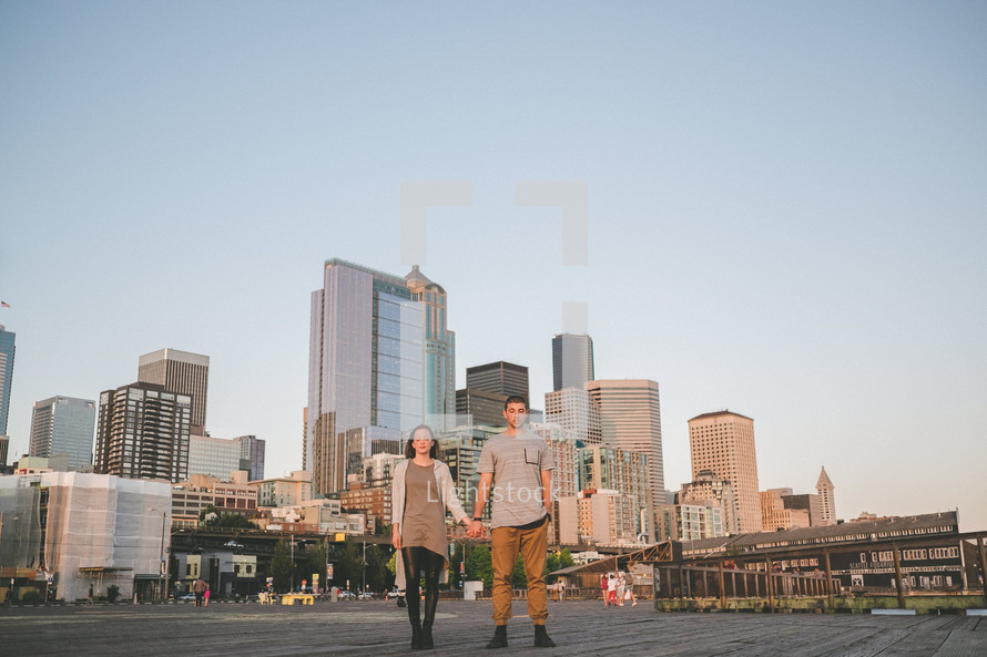A man and woman holding hands with skyscrapers behind them.