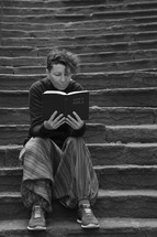 woman sitting alone on stone steps reading a Bible 