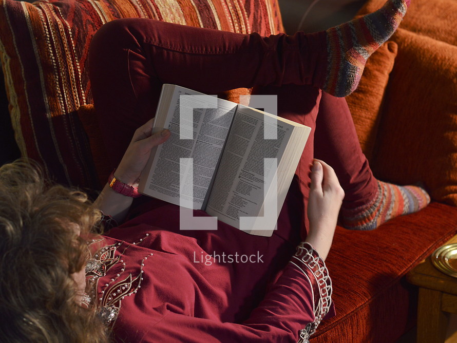 woman reading her bible comfortably on a sofa at home 