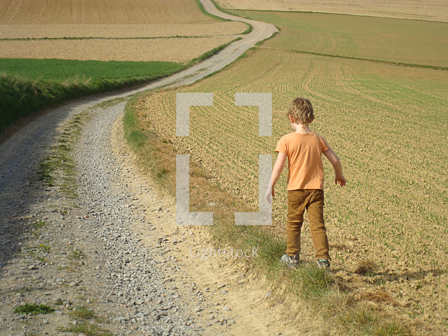 Child walking along a winding road through the countryside.
