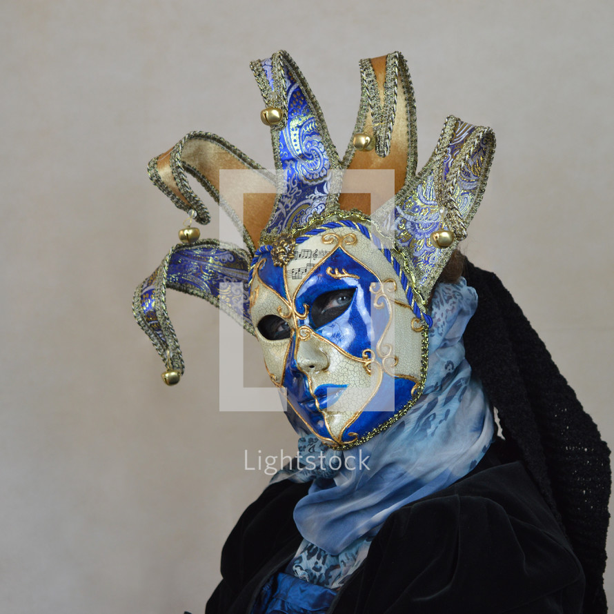 masquerade mask - woman disguised with blue, white and golden Venetian mask looking provocative in front of neutral light background