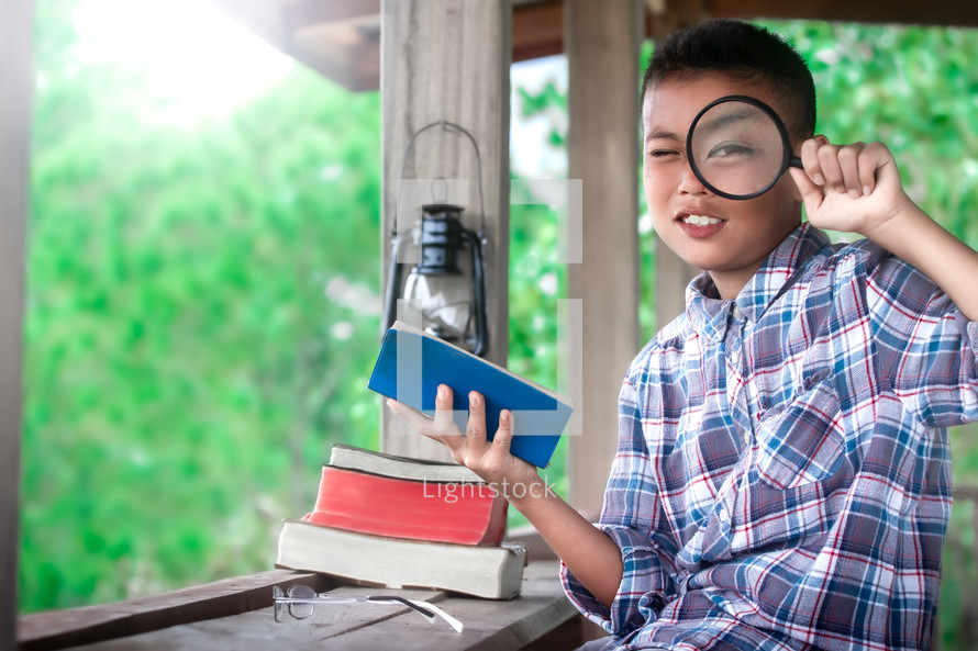 a boy reading a Bible outdoors holding a magnifying glass 