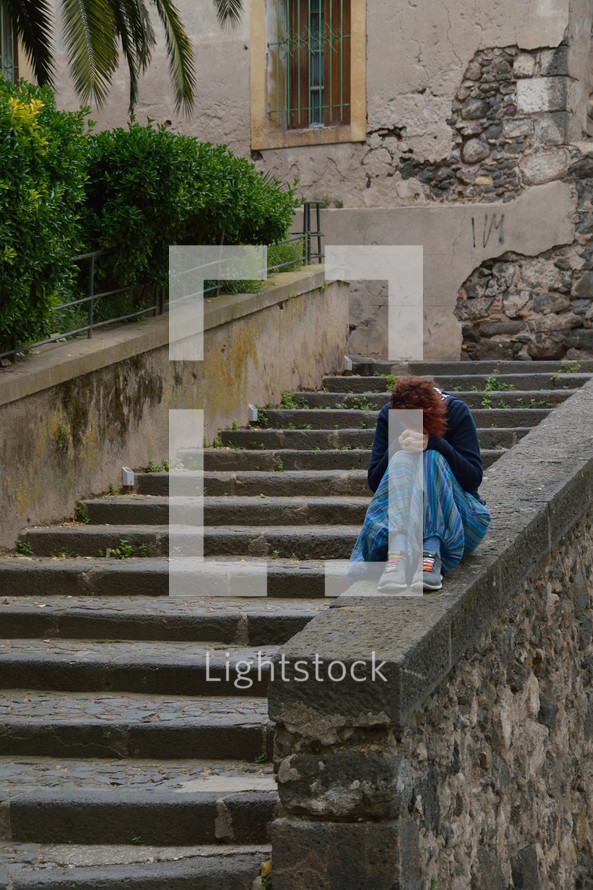 a sad young woman sitting along on concrete steps 