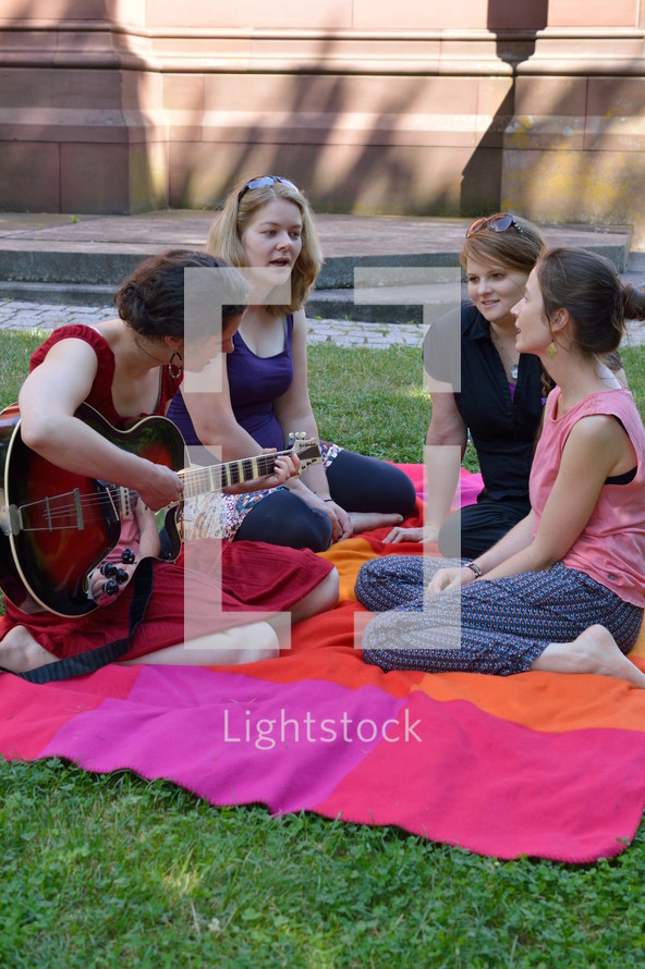 friends sitting on a blanket in the grass singing songs of praise 
