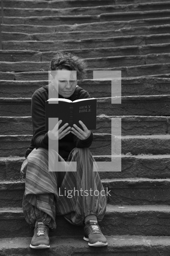 woman sitting alone on stone steps reading a Bible 