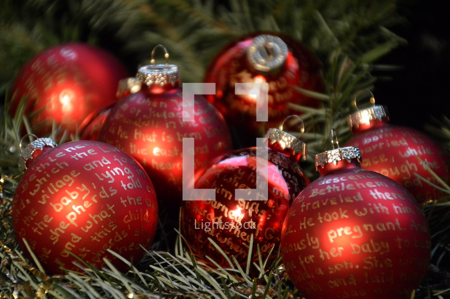 Red Christmas balls with gold lettering on evergreen boughs.