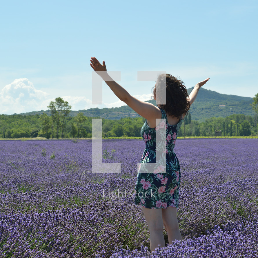 woman standing in a field of lavender with arms raised 