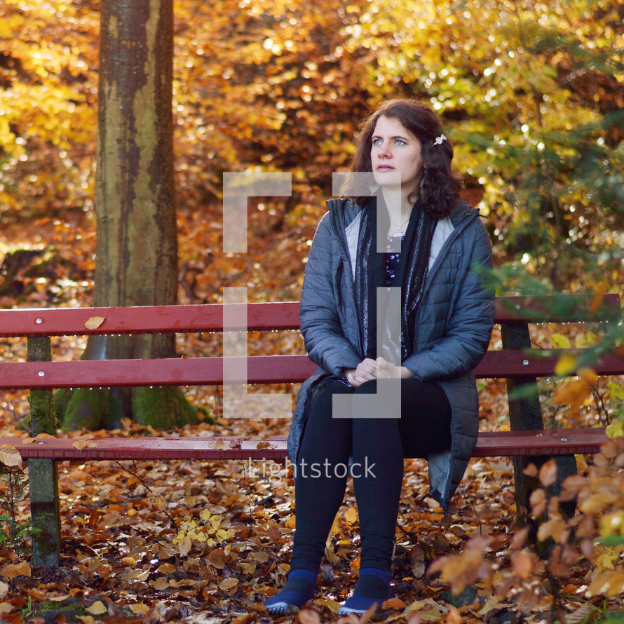 a woman sitting on a bench praying in fall 