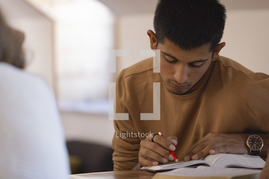 Young man reading and marking his Bible at a desk