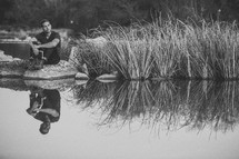 A man sitting at the shore of a pond with a Bible 