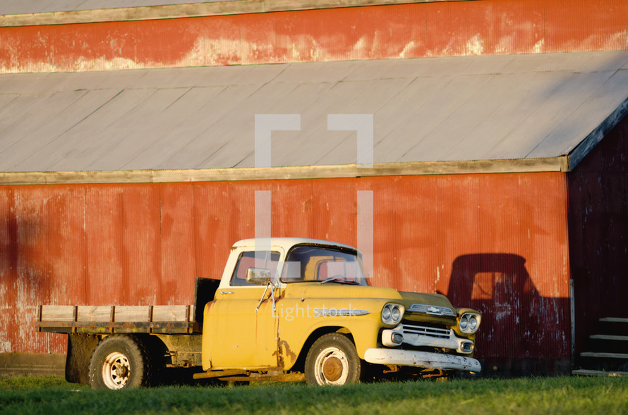 old flatbed truck parked in front of a red barn