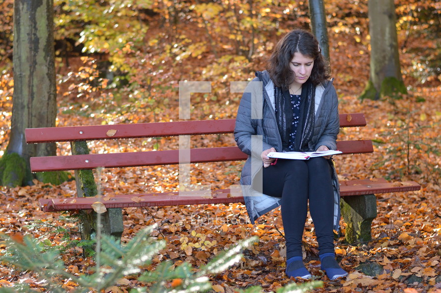 a woman reading on a bench in a park in fall 