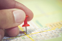 Hand holding a pin on a map