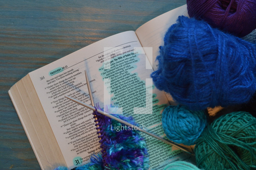 wool and a piece of knitting on a bible open at the page of Proverbs 31: The Wife of Noble Character with the line: She selects wool and flax marked 