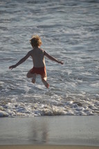 Little boy jumping in the waves with flying hair and having fun