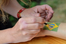 woman painting a brazilian flag on someones arm. 