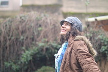 a smiling woman in coat and hat looking up to God 