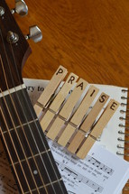 part of a guitar with the letters PRAISE burned into wooden clothespins and sheets of music