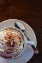 Whipped cream on top of a pot with hot chocolate on a wooden table