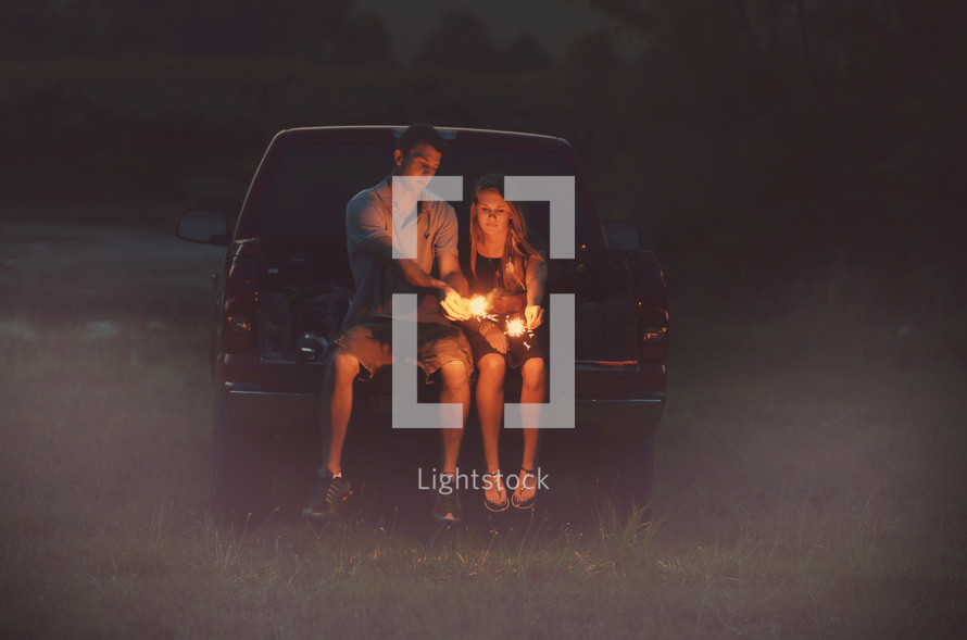 couple lighting sparklers on a tailgate 