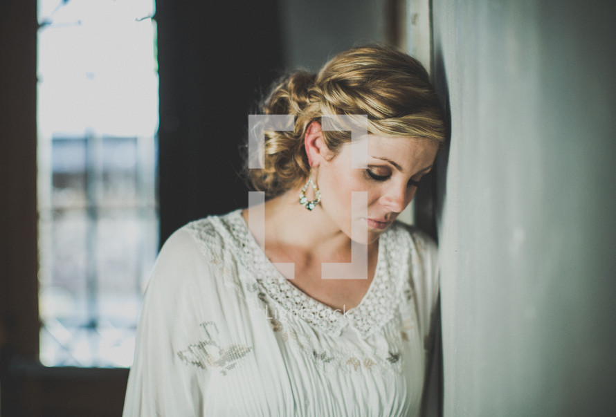 Pensive woman leaning against a wall.