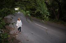 Woman walking on a country road lined with trees.