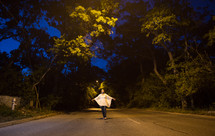Woman walking in the middle of the road at night withy arms wide open.