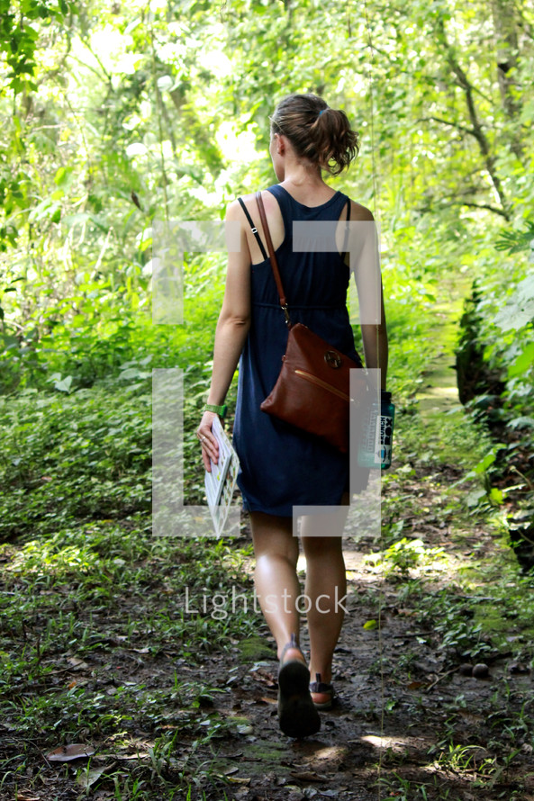 a woman walking into the woods carrying a journal and purse