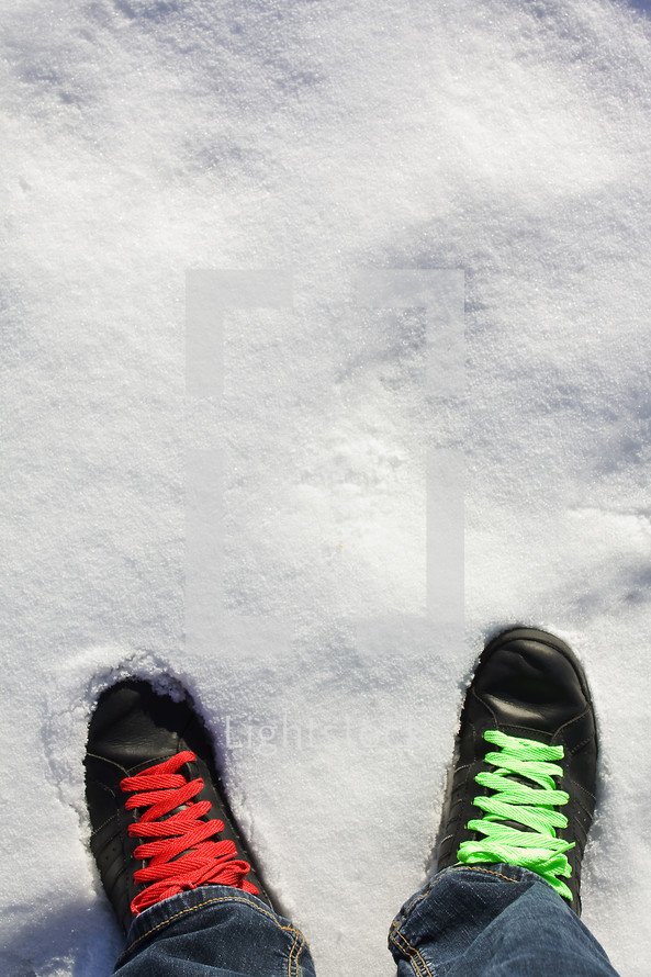 green and red shoe laces on a pair of black shoes standing in the snow