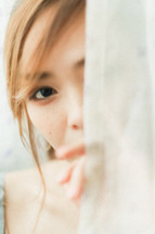 shy teen girl hiding behind a curtain 