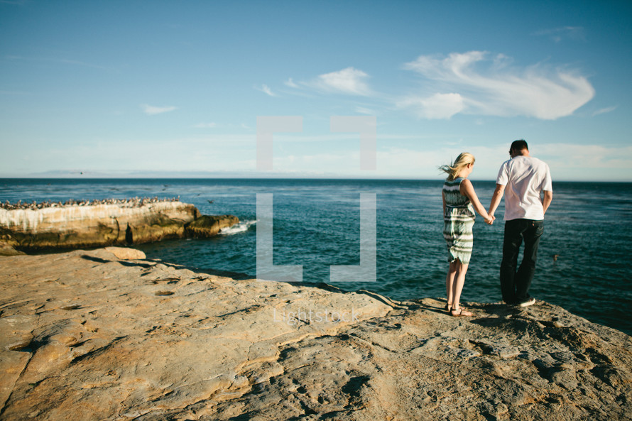 couple holding hands standing on a rocky shore 