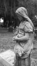 A stone statue of a weeping woman watching over a grave in a cemetery filled with tomb stones of those dearly departed.

