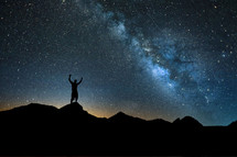 silhouette of a man with raised arms standing under stars in the night sky