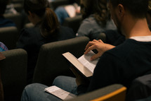 man turning the pages of a Bible at a worship service 