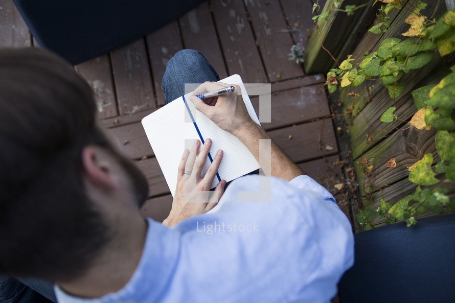 a man writing in a journal outdoors 