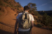 Hiker with a backpack walking on a hillside dirt path.