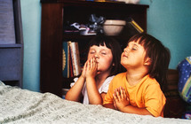 young children praying beside of their bed 