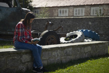 Young woman sitting outside on rock wall reading her Bible with stone buildings in the background