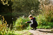 a boy playing with a stick near a pond 