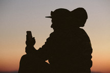 silhouette of a man with a backpack looking at his cellphone at sunset 