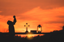 silhouette of a boy reading a bible and praying with Oil lamp on wood at sunset against an orange sky 