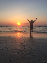 silhouette of a man with raised arms on a beach at sunset 