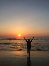 silhouette of a man with raised hands on a beach at sunset 