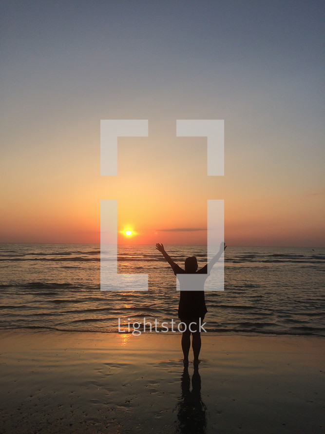 silhouette of a man with raised hands on a beach at sunset 