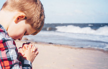 boy child praying on a beach 