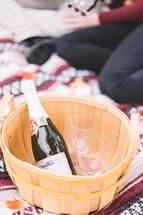 champagne and glasses in a basket on a blanket 