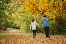 couple walking holding hands through fall leaves 